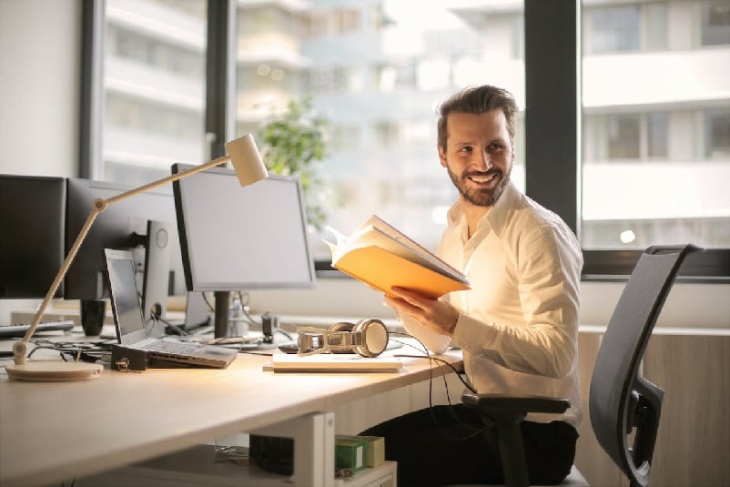 Man holding folder, sitting at desk with computer